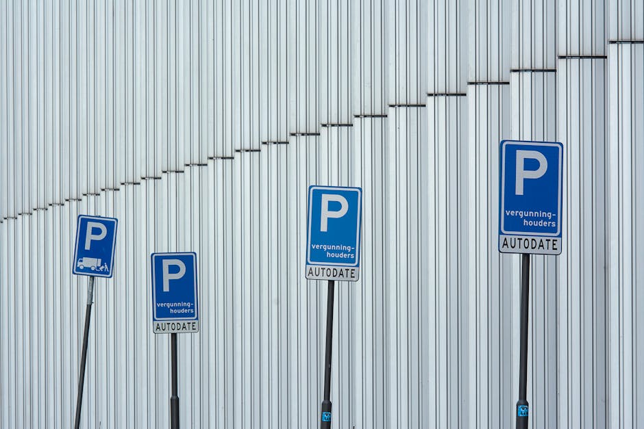 Four blue parking permit signs mounted on black metal poles stand in front of a modern, vertically ribbed metallic wall. The signs display a large white 'P' and include the words 'vergunning-houders' and 'AUTODATE', indicating designated parking areas for vehicles involved in house removals or furniture transport. Each sign varies slightly in tilt and height, with some positioned closer to the viewer and others further away. The environment appears to be outdoors, with natural lighting highlighting the sheen of the metallic wall and the reflective surfaces of the signs. This setup reflects parking regulations relevant to relocation services, such as those offered by Man with Van Sudbury, supporting efficient home relocation and packing logistics without obstructing access for loading or unloading furniture and appliances.